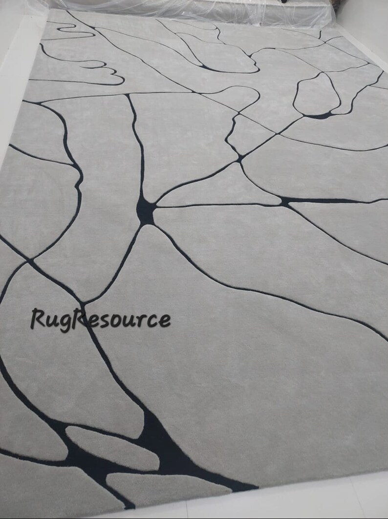 Puede incluir: Una alfombra gris claro con un dise&ntilde;o abstracto negro. El dise&ntilde;o presenta una red de l&iacute;neas y formas que se asemejan a venas o ramas. La alfombra est&aacute; hecha de un material suave y mullido y tiene un estilo moderno y contempor&aacute;neo. Rugresource est&aacute; impreso en la esquina inferior izquierda de la alfombra.