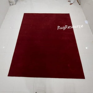 May include: A solid red rug with a subtle texture. The rug is laid out on a white tiled floor. The text "RugResource" is visible in the bottom right corner of the image.