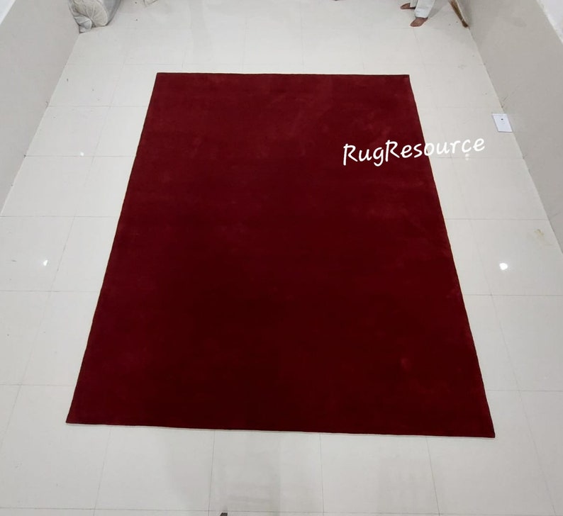 May include: A solid red rug with a subtle texture. The rug is laid out on a white tiled floor. The text "RugResource" is visible in the bottom right corner of the image.
