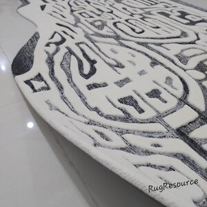 May include: A white and gray area rug with an abstract design. The rug has a thick, plush pile and a fringed edge.