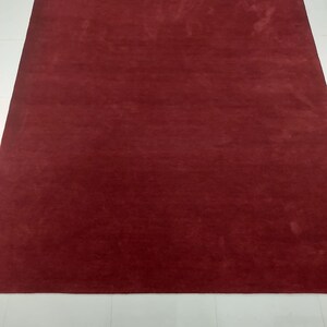 May include: A solid red rug with a subtle texture. The rug is laid out on a white tiled floor. The text "RugResource" is printed in white on the rug.