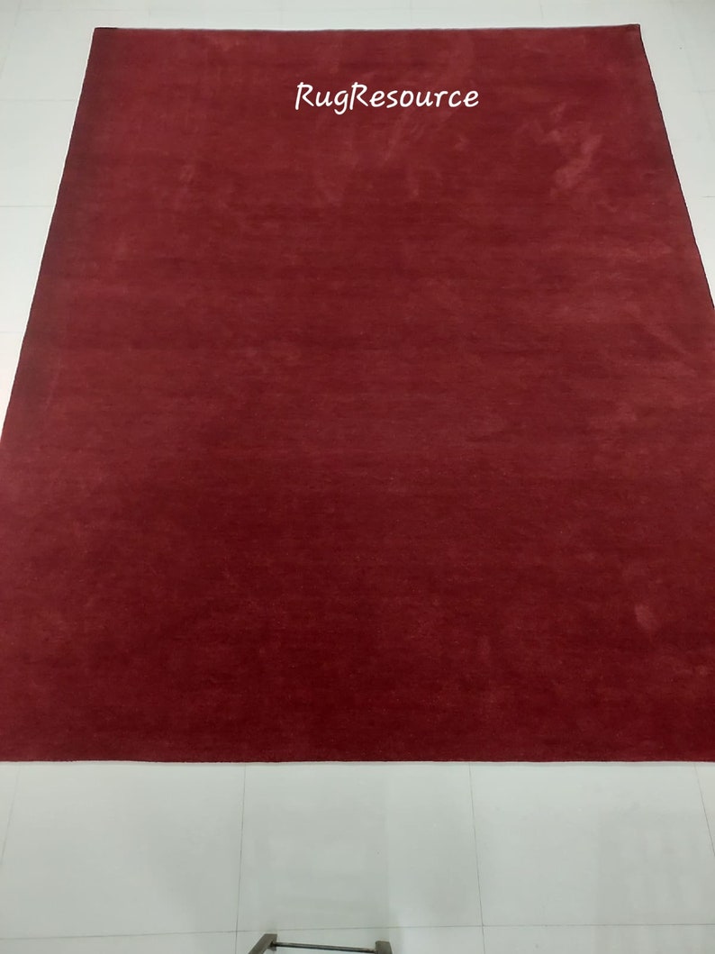 May include: A solid red rug with a subtle texture. The rug is laid out on a white tiled floor. The text "RugResource" is printed in white on the rug.
