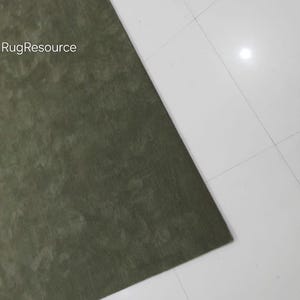 May include: A section of a green rug with a textured surface. The rug is positioned diagonally against a white tiled floor. The text "RugResource" is visible in the upper left corner.