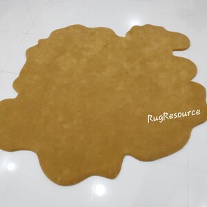 May include: A large, mustard yellow, shag rug with an irregular, organic shape. The rug is made of soft, plush fibers and has a unique, modern design.