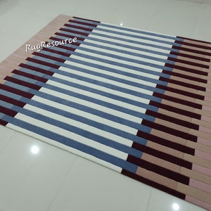 May include: A striped rug with a geometric pattern in shades of pink, beige, blue, and burgundy. The rug has a modern design and is perfect for adding a touch of color and style to any room.
