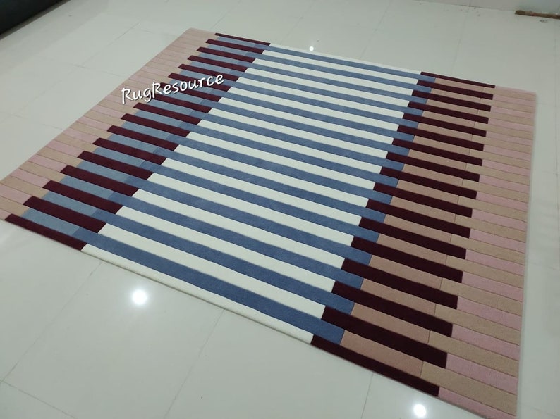 May include: A striped rug with a geometric pattern in shades of pink, beige, blue, and burgundy. The rug has a modern design and is perfect for adding a touch of color and style to any room.
