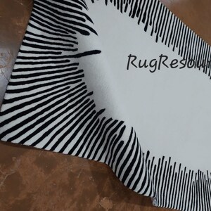 May include: A black and white striped rug with a circular design in the center. The rug is folded in half and the edges are visible. The rug is made of a soft, plush material.