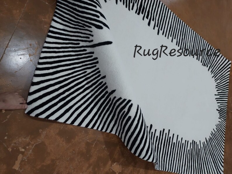 May include: A black and white striped rug with a circular design in the center. The rug is folded in half and the edges are visible. The rug is made of a soft, plush material.