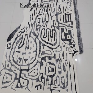 May include: Abstract black and white area rug with a geometric design. The rug has a unique shape and is made of a soft, plush material.