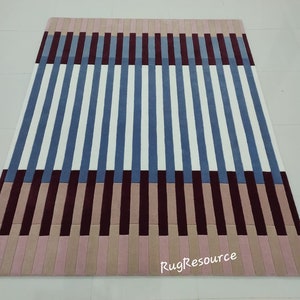 May include: A striped rug with blue, white, burgundy, and pink stripes. The rug has a modern design and is made of a soft, plush material. The rug is available in a variety of sizes.