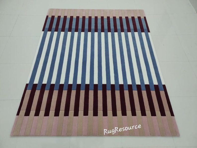 May include: A striped rug with blue, white, burgundy, and pink stripes. The rug has a modern design and is made of a soft, plush material. The rug is available in a variety of sizes.