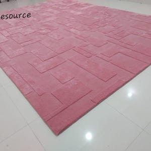 May include: A pink area rug with a geometric pattern. The rug has a raised texture and a soft, plush feel.