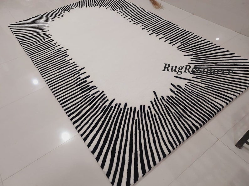 May include: A white rug with a black oval border made of vertical lines. The rug has a modern design.