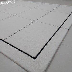 Pu&ograve; includere: Un tappeto rettangolare bianco con bordo nero e motivo a griglia. Il tappeto ha una consistenza morbida ed &egrave; realizzato in un materiale morbido. Il tappeto &egrave; adatto per soggiorni, camere da letto o ingressi.