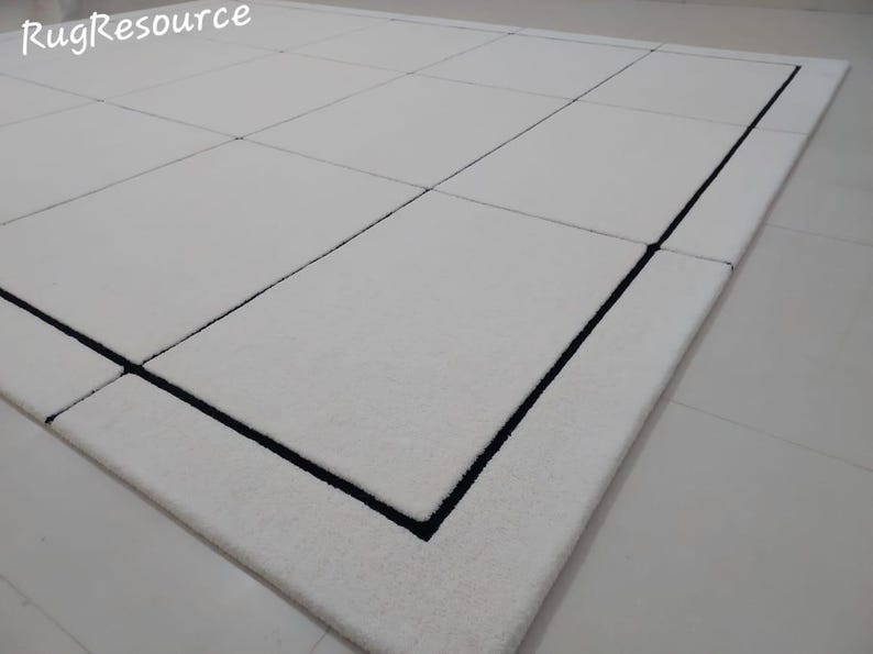 Pu&ograve; includere: Un tappeto rettangolare bianco con bordo nero e motivo a griglia. Il tappeto ha una consistenza morbida ed &egrave; realizzato in un materiale morbido. Il tappeto &egrave; adatto per soggiorni, camere da letto o ingressi.