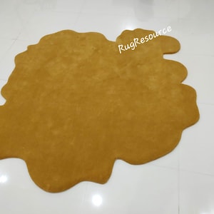 May include: A large, mustard yellow, shag rug with an irregular, abstract shape. The rug is on a white tiled floor.