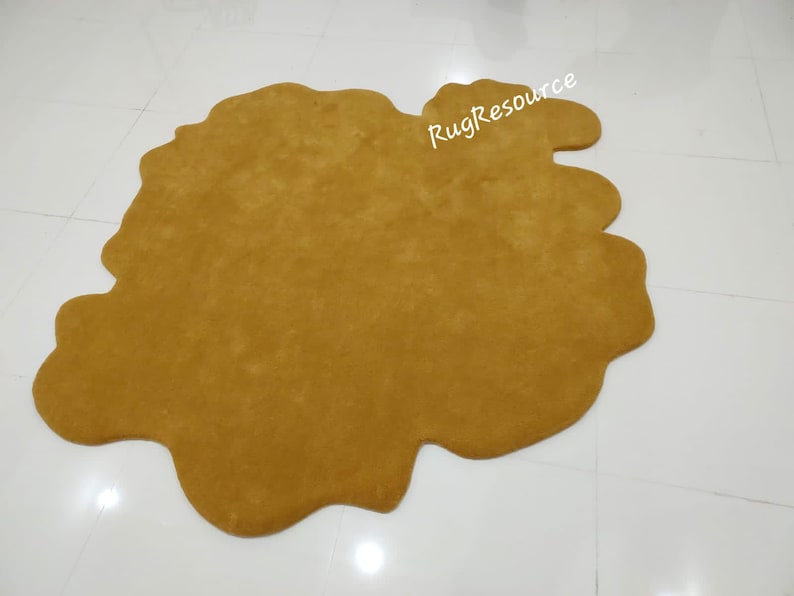 May include: A large, mustard yellow, shag rug with an irregular, abstract shape. The rug is on a white tiled floor.