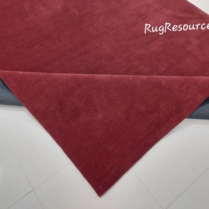 May include: Close-up of a burgundy red rug with a gray backing. The rug is folded in half, revealing the backing.