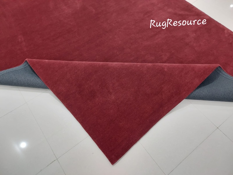 May include: Close-up of a burgundy red rug with a gray backing. The rug is folded in half, revealing the backing.