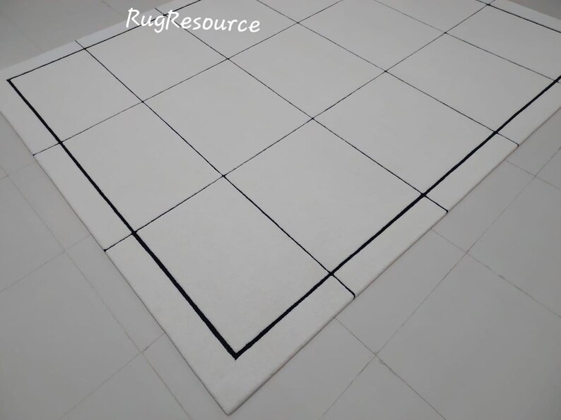 Pu&ograve; includere: Un tappeto bianco con un motivo a griglia, con linee nere che creano un design geometrico. Il tappeto ha un bordo e il testo "RugResource" &egrave; visibile nell'angolo in alto a sinistra.