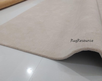 May include: A close-up of a light beige rug with a slightly wavy edge. The rug is made of a soft, plush material and has a subtle texture. The text "RugResource" is visible in the bottom right corner of the image.