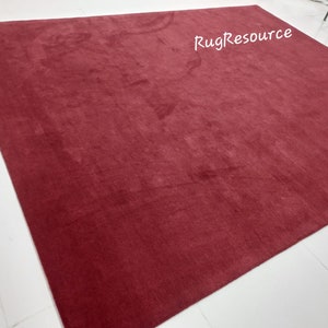 May include: A solid red rug with a soft, plush texture. The rug is laid out flat on a white tiled floor. The text "RugResource" is visible in the upper right corner of the rug.