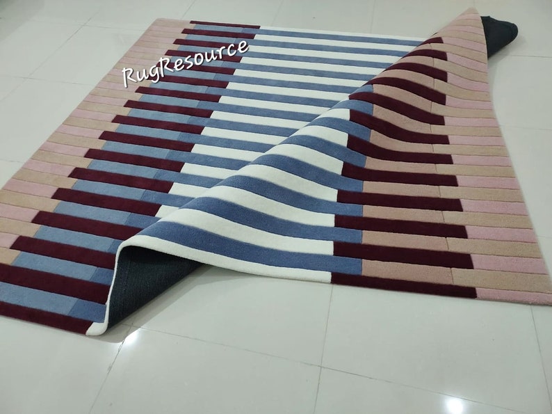May include: A white, blue, and pink striped rug with a geometric pattern. The rug is folded in half and the underside is visible. The rug is made of a soft, plush material.