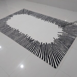 May include: A white rug with a black and white striped border. The stripes are arranged in a radial pattern, creating a sunburst effect. The center of the rug is white.