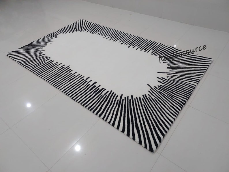 May include: A white rug with a black and white striped border. The stripes are arranged in a radial pattern, creating a sunburst effect. The center of the rug is white.