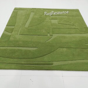May include: A green area rug with a modern abstract design. The rug has a raised texture and a subtle sheen.
