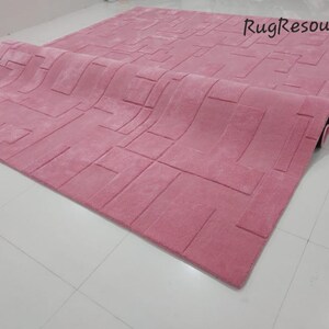 May include: A pink area rug with a geometric pattern. The rug is rolled up and the edge of the rug is visible.