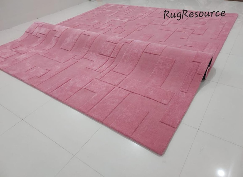 May include: A pink area rug with a geometric pattern. The rug is rolled up and the edge of the rug is visible.