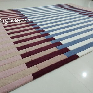 May include: A striped rug with pink, beige, burgundy, and blue stripes. The rug is made of a soft, plush material and has a modern design.