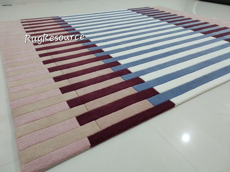 May include: A striped rug with pink, beige, burgundy, and blue stripes. The rug is made of a soft, plush material and has a modern design.