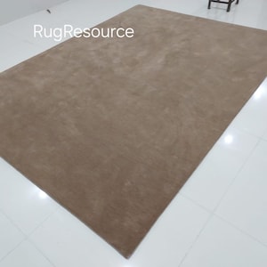 May include: A large, rectangular, light brown rug with a subtle texture. The rug is laid out on a white tiled floor. The text "RugResource" is visible in the top left corner of the image.