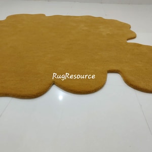 May include: A large, mustard yellow, shag rug with an irregular, organic shape. The rug is made of soft, plush fibers and has a slightly raised edge.