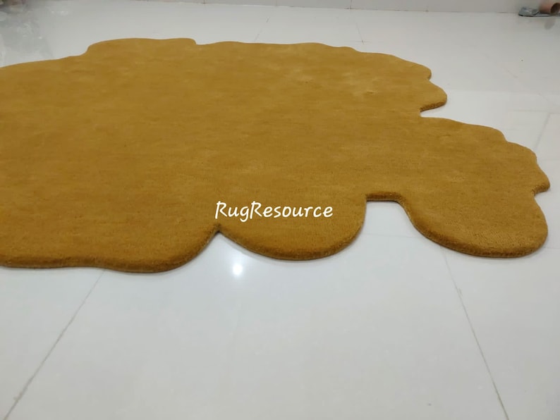 May include: A large, mustard yellow, shag rug with an irregular, organic shape. The rug is made of soft, plush fibers and has a slightly raised edge.