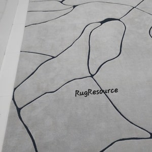Puede incluir: Una alfombra gris con un dise&ntilde;o abstracto negro. El dise&ntilde;o se asemeja a una red de venas o r&iacute;os. La alfombra tiene una textura suave y mullida.