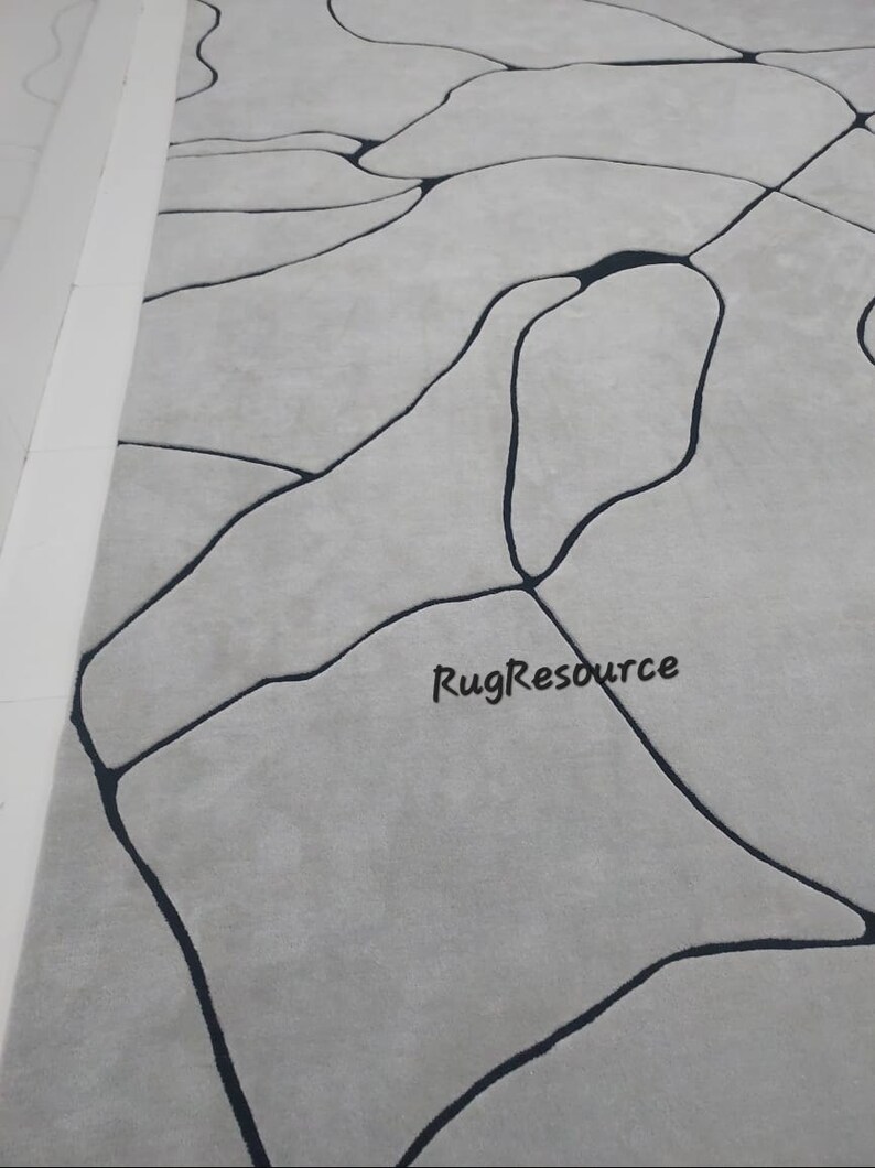 Puede incluir: Una alfombra gris con un dise&ntilde;o abstracto negro. El dise&ntilde;o se asemeja a una red de venas o r&iacute;os. La alfombra tiene una textura suave y mullida.