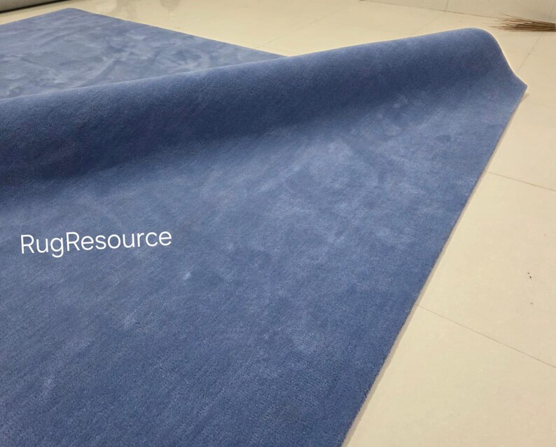 May include: A rolled-up, solid blue rug with a soft, textured surface. The rug is displayed on a light-colored tiled floor. The text "RugResource" is visible in the lower left corner.