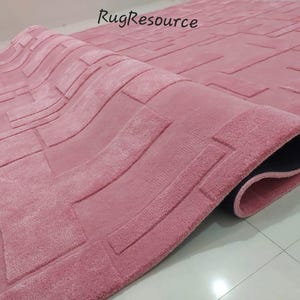 May include: A pink rug with a geometric pattern. The rug has a raised texture and a black backing.