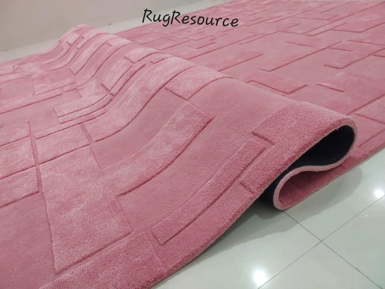 May include: A pink rug with a geometric pattern. The rug has a raised texture and a black backing.