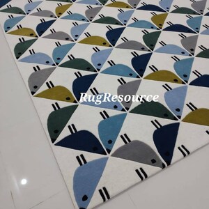 May include: A white rug with a geometric pattern of blue, green, and yellow birds. The rug has a modern design and is perfect for a child's room or play area.