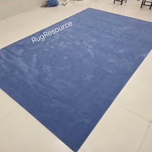 May include: A large, rectangular blue rug with a textured surface. The rug is placed on a tiled floor. The text "RugResource" is visible in the upper left corner. This rug is suitable for living rooms, bedrooms, or other spaces.