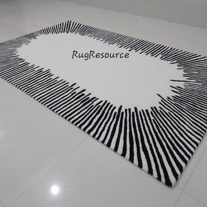 May include: A white rug with a black oval border. The border is made up of thin, vertical lines that radiate outwards from the center of the oval. The text "RugResource" is printed in black on the white background.