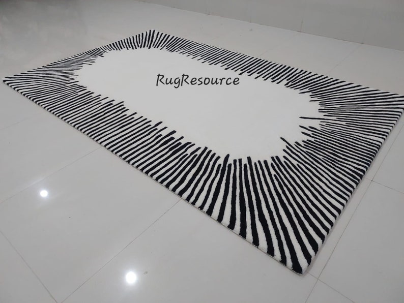 May include: A white rug with a black oval border. The border is made up of thin, vertical lines that radiate outwards from the center of the oval. The text "RugResource" is printed in black on the white background.