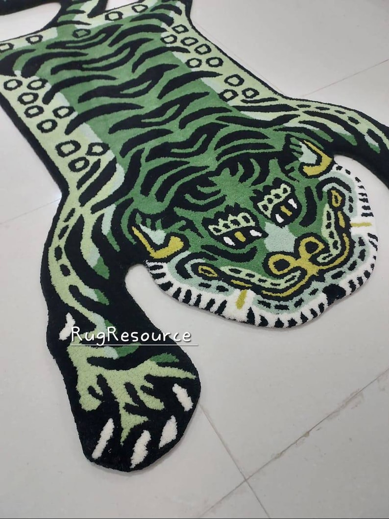 Op de afbeelding: Een groen en zwart tapijt in de vorm van een tijger met een gedetailleerd ontwerp. Het tapijt heeft een tijgergezicht en -lichaam met strepen en vlekken. Het tapijt is gemaakt van een zacht, pluche materiaal en is geschikt voor een woon- of slaapkamer.