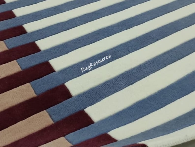May include: A close-up of a striped rug with alternating bands of white, blue, burgundy, and beige. The rug has a soft, plush texture.