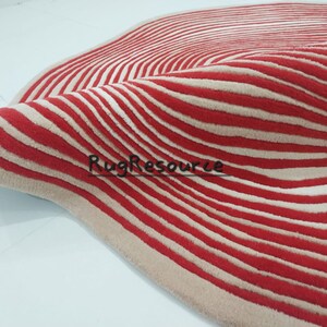 May include: A red and cream striped rug with a wavy pattern. The rug is made of a soft, plush material.