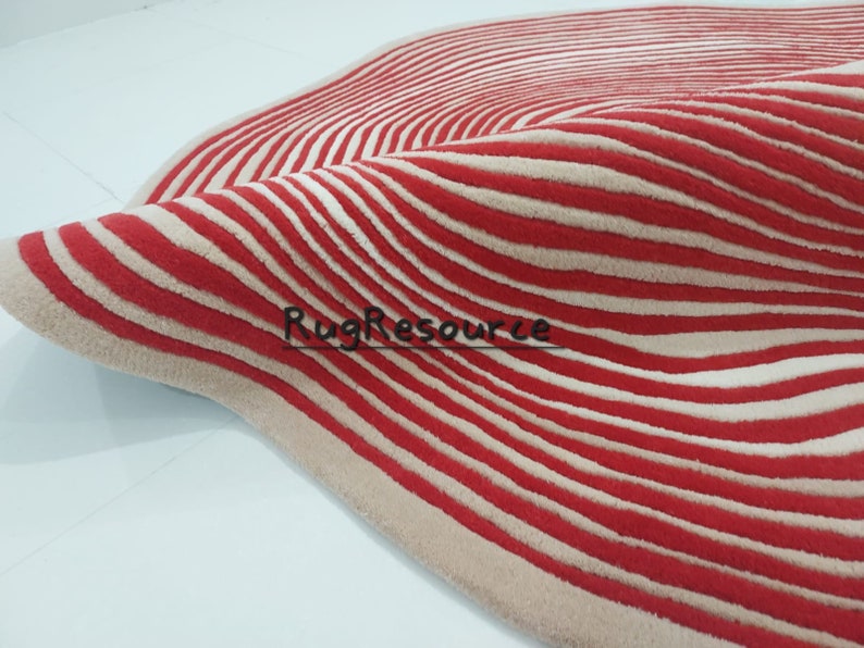 May include: A red and cream striped rug with a wavy pattern. The rug is made of a soft, plush material.
